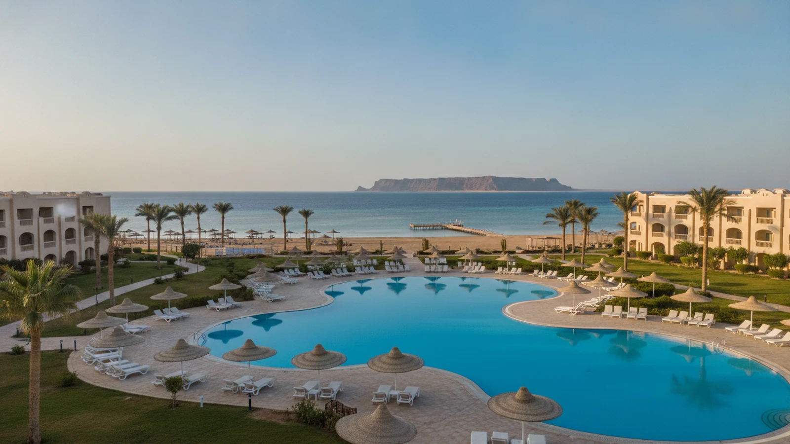 Resort v Nabq Bay s velkým bazénem, palmami a pláží s molem, v dálce ostrov Tiran