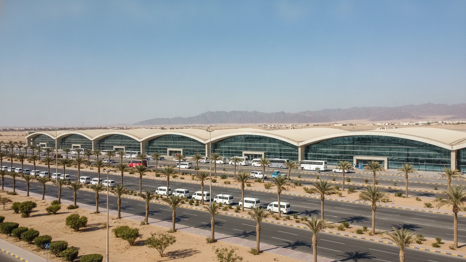 Odbavovací budova letiště Hurghada s palmami, minibusy a horami v pozadí