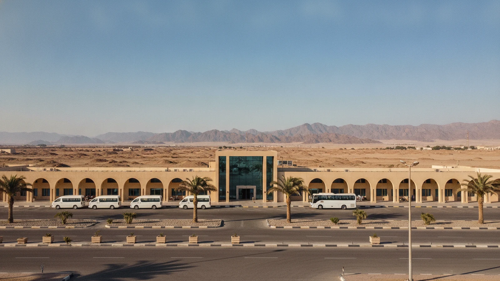 Odbavovací budova letiště Marsa Alam s palmami, minibusy a pouští za terminálem