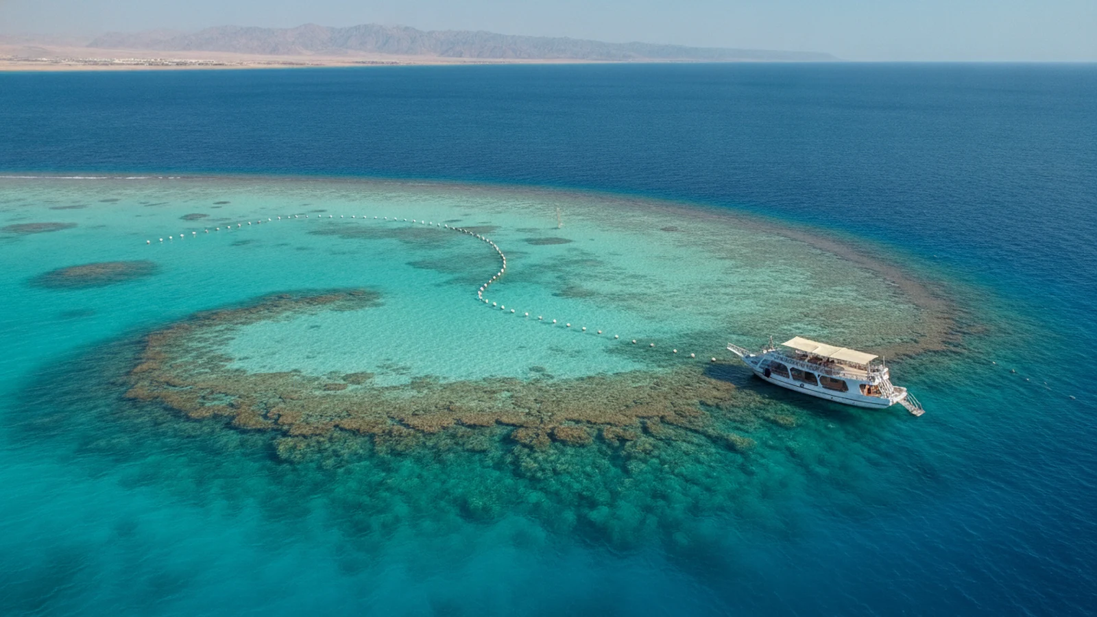 Laguna útesu Samadai u Marsa Alamu s bójemi vyznačujícími zóny a výletní lodí na okraji útesu