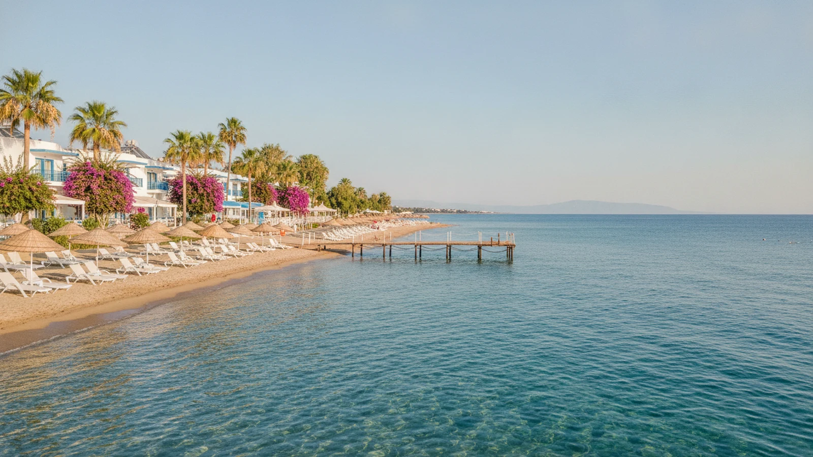 Písečná pláž s lehátky a molem před hotelovým resortem u Turgutreisu na poloostrově Bodrum