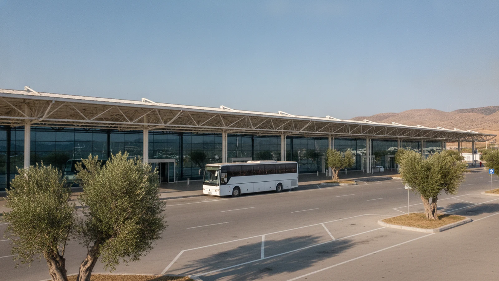 Prostranství před mezinárodním terminálem letiště Milas-Bodrum s letištním autobusem a olivovníky
