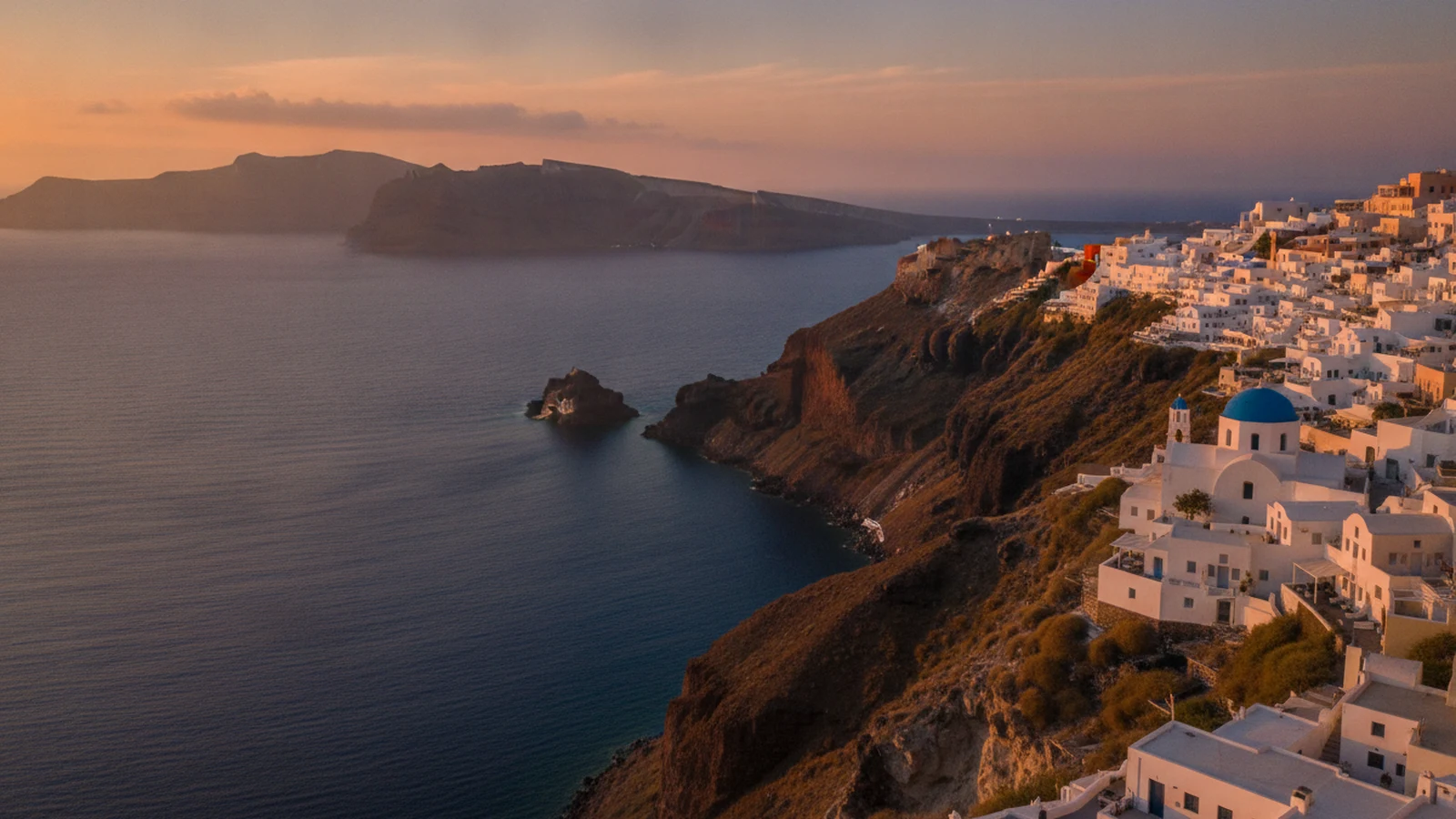 Bílé domy a kaple s modrou kopulí na hraně kaldery v Imerovigli na Santorini, v pozadí skála Skaros a ostrůvek Nea Kameni