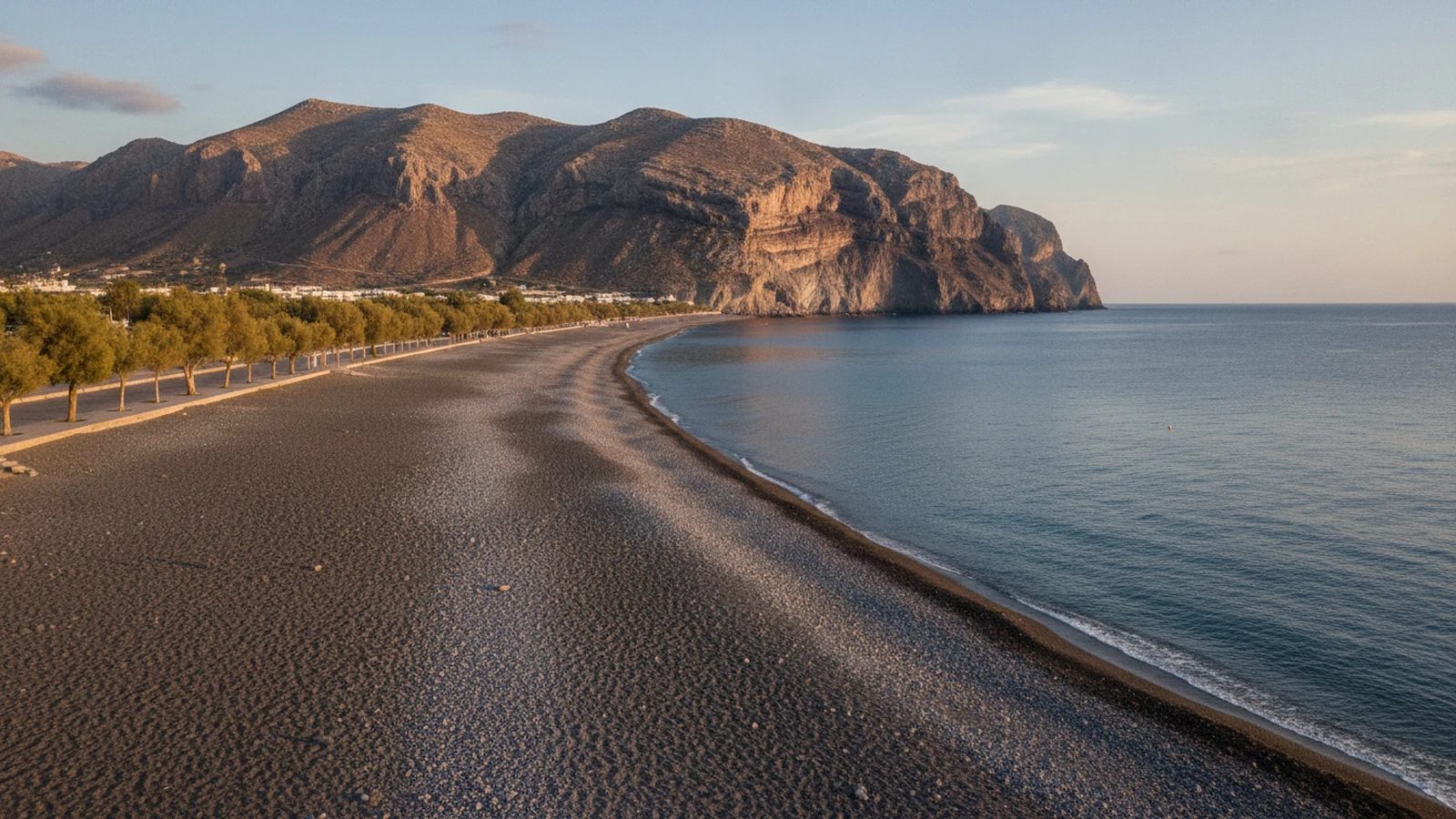 Pláž Kamari na Santorini s černým sopečným pískem, tamaryšky u promenády a skalním masivem Mesa Vouno